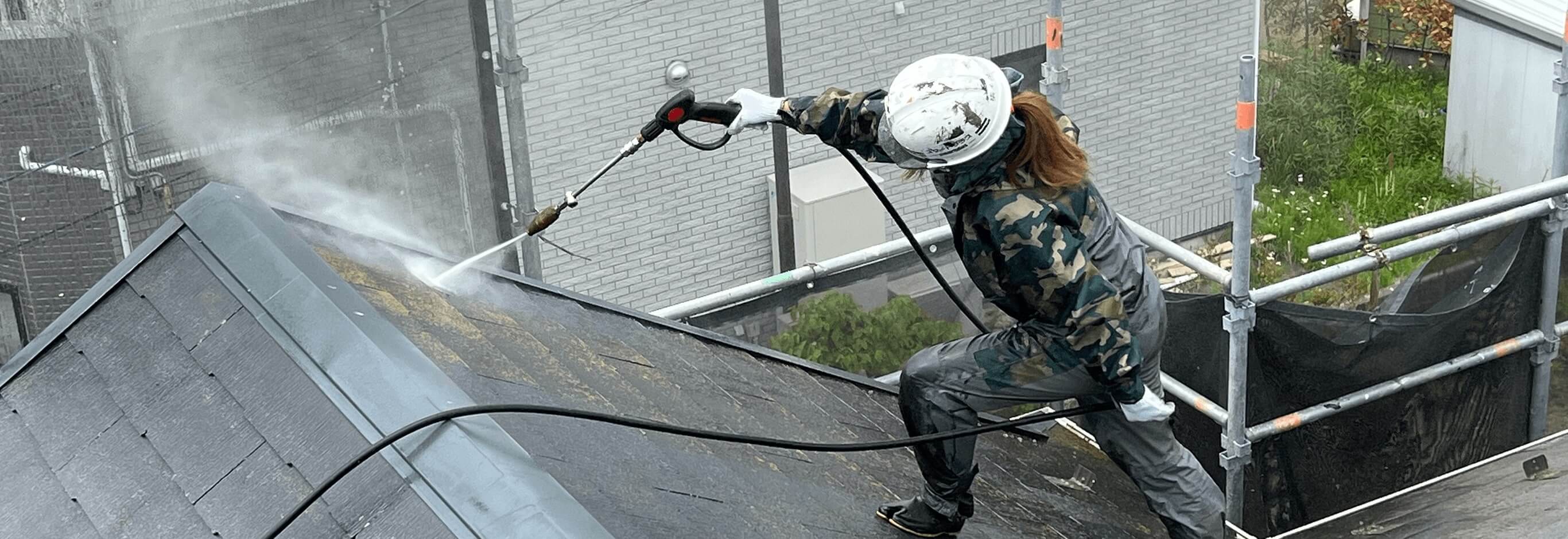 女性作業員が屋根に水をジェットでかけている写真
